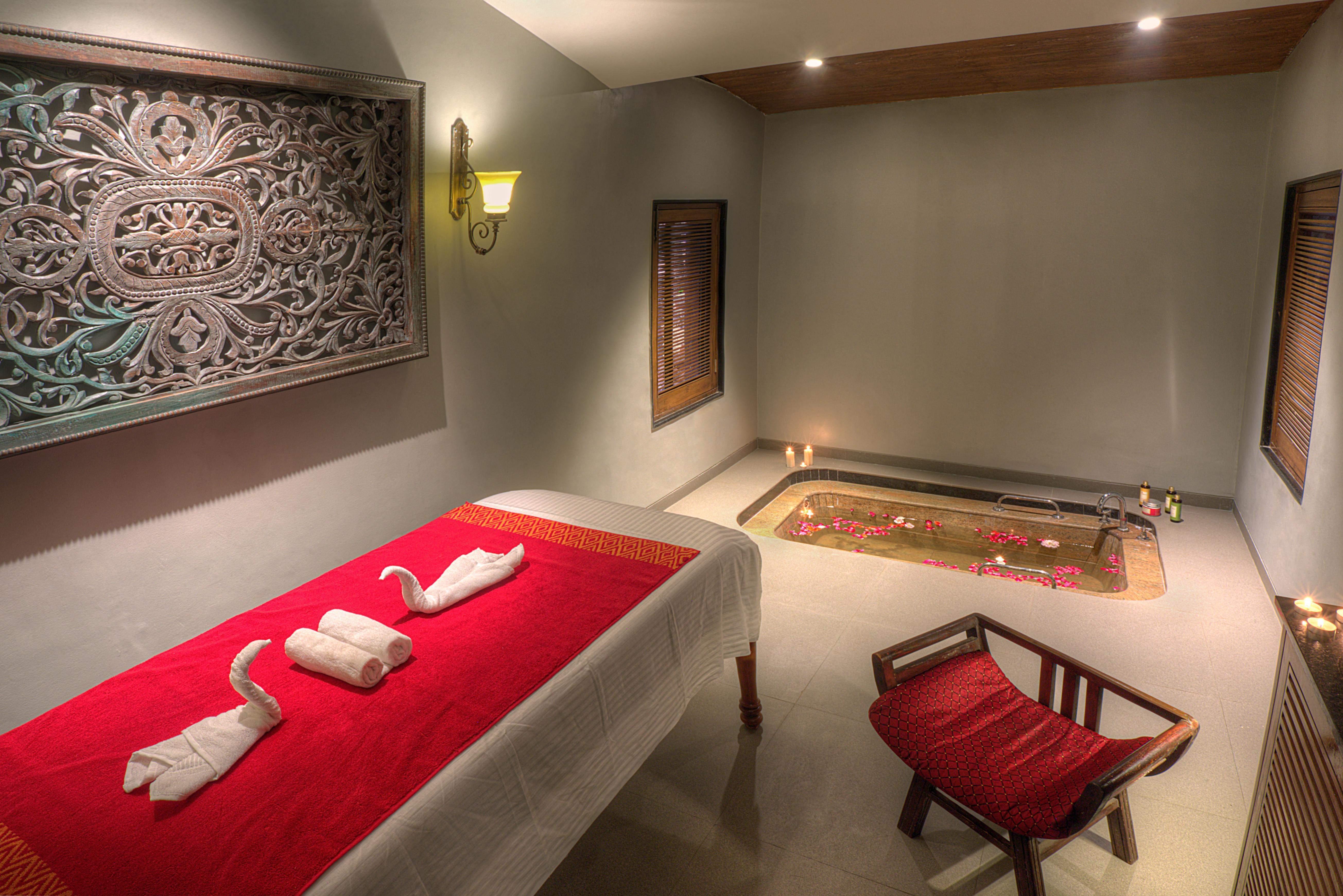 A relaxing spa room at Ramsukh Resort, featuring a massage bed, warm lighting, artistic wall decor, and a small flower-filled water bath.